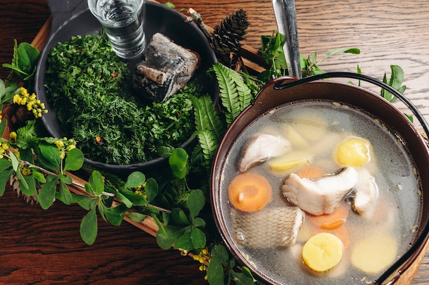 Russische traditionelle Fischsuppe in einer Schüssel Ukha serviert mit Glut und Wodka auf Holzbrett Fischbrühe Traditionelle Küche in Russland