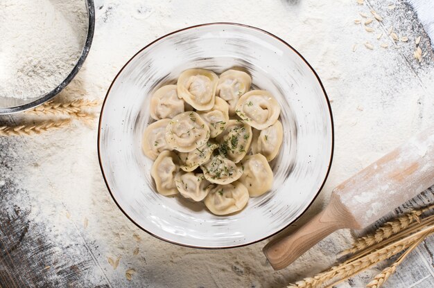 Russische traditionelle Pelmeni mit Fleisch auf einem weißen Teller. Weizenspitzen auf einem Holzbrett