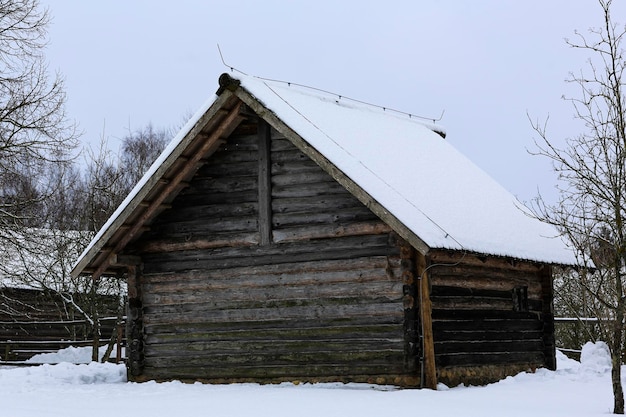 Russische Winterlandschaft Eine alte Holzhütte ein Blockhaus mit Strohdach Verlassenes russisches Dorf mit Schnee bedeckt Blockhaus mit Scheune