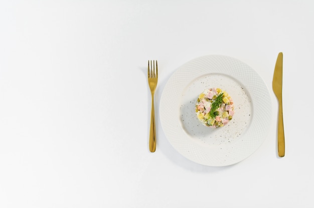 Russischer Salat auf einer weißen Platte mit einem goldenen Messer und einer Gabel
