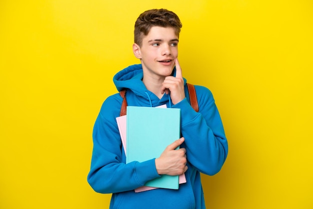 Russischer Student des Teenagers lokalisiert auf gelbem Hintergrund, der eine Idee beim Nachschlagen denkt