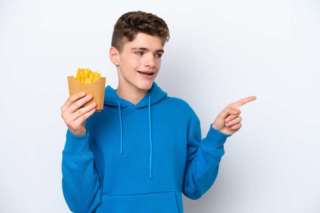 Russischer Teenager, der Bratkartoffeln isoliert auf weißem Hintergrund hält, mit dem Finger zur Seite zeigt und ein Produkt präsentiert