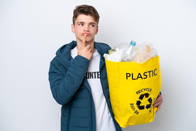 Russischer Teenager, der eine Tüte voller Plastikflaschen hält, um sie auf weißem Hintergrund zu recyceln, hat Zweifel, während er nach oben schaut