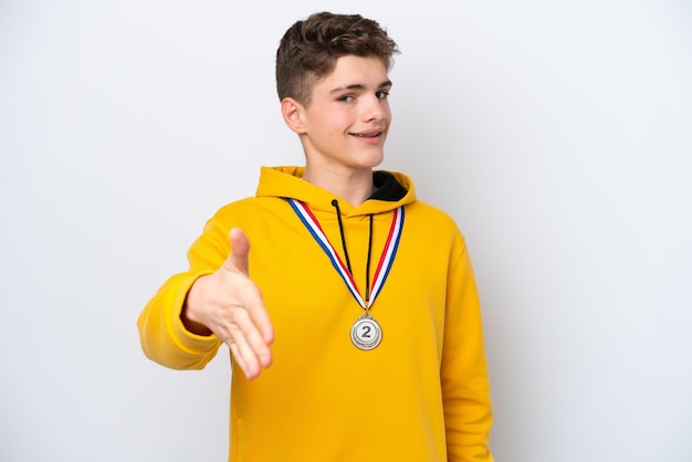 Russischer Teenager mit Medaillen isoliert auf weißem Hintergrund, der sich die Hände schüttelt, um ein gutes Geschäft abzuschließen
