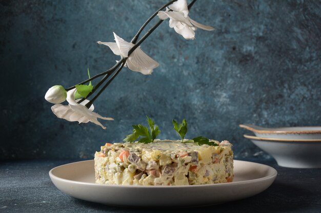 Russischer traditioneller Salat "Olivier" mit Gemüse und Fleisch und Mayonnaise. Wintersalat. Salat auf einer Platte/oder Glasschüssel, auf einem grauen Steinhintergrund.