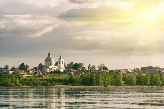 Russisches Dorf mit der orthodoxen Kirche in der Nähe des sonnigen Flusses