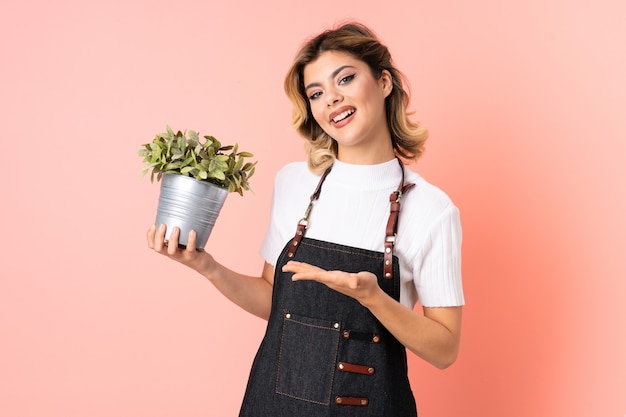 Russisches Gärtnermädchen, das eine Pflanze lokalisiert hält, die auf rosa hält Copyspace imaginär auf der Handfläche hält