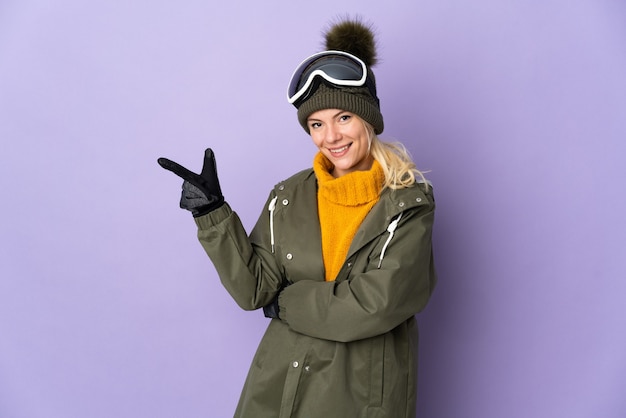 Russisches Mädchen des Skifahrers mit Snowboardbrille lokalisiert auf lila Hintergrund, der Finger zur Seite zeigt