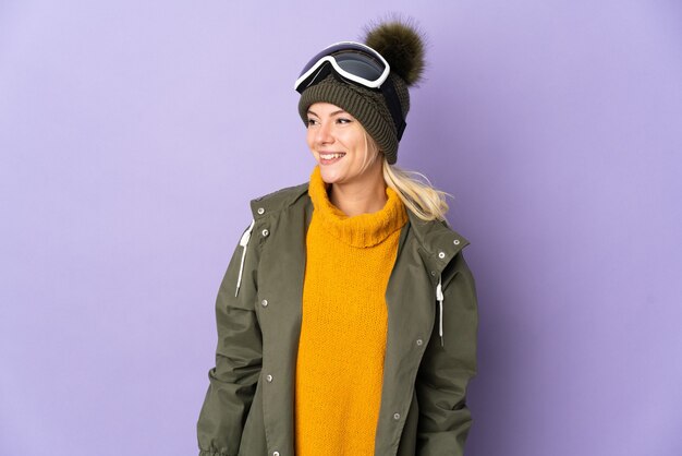 Russisches Mädchen des Skifahrers mit Snowboardbrille lokalisiert auf lila Hintergrund schauender Seite