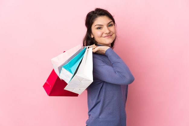 Russisches Mädchen des Teenagers lokalisiert auf rosa Wand, die Einkaufstaschen hält und lächelt