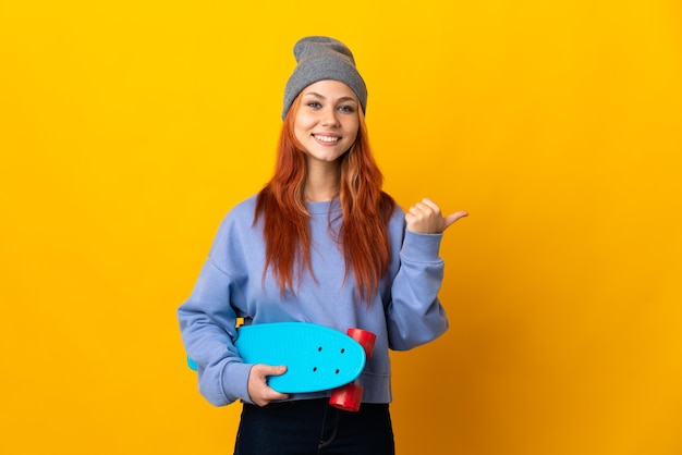 Russisches Skater-Mädchen des Teenagers lokalisiert auf gelber Wand, die zur Seite zeigt, um ein Produkt zu präsentieren