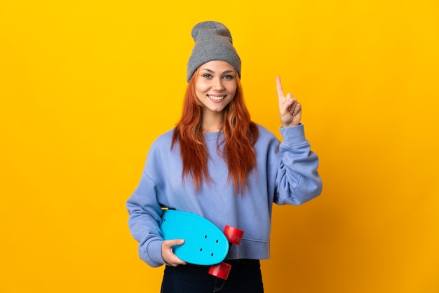 Russisches Skatermädchen des Teenagers lokalisiert auf gelbem Hintergrund, das auf eine großartige Idee zeigt