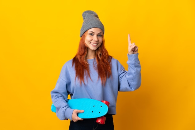 Russisches Teenager-Skater-Mädchen auf gelbem Zeigen und Anheben eines Fingers im Zeichen des Besten