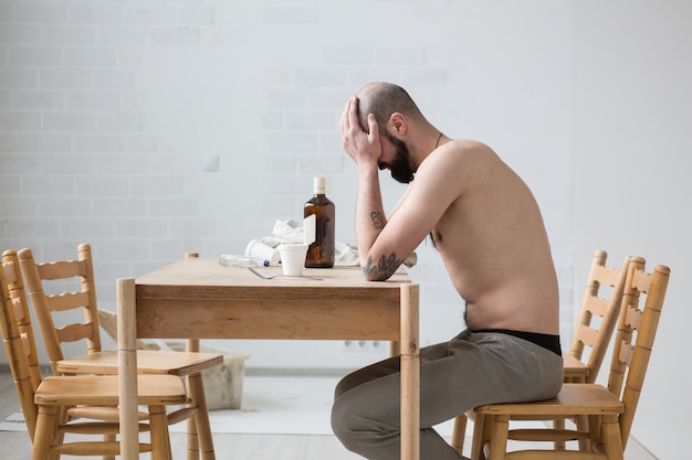 Russo bêbado sentado à mesa e triste. ela fecha o rosto