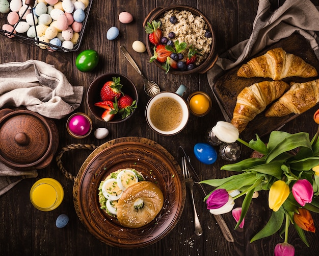 Rústico desayuno de pascua con huevos bagels, tulipanes, croissants, huevo, avena con bayas, huevos de codorniz de colores y decoraciones de vacaciones de primavera. Vista superior