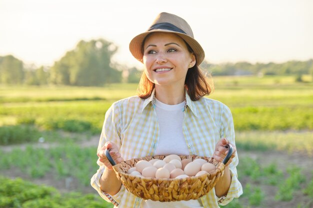 Rústico retrato de mujer madura con canasta de huevos en la pradera