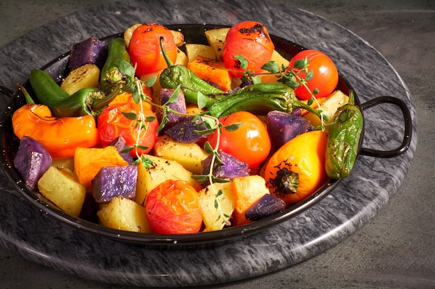 Rústico, verduras al horno en una fuente para horno. Comida vegetariana vegetariana estacional en tablero de piedra oscura
