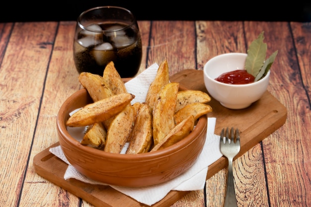 Rustikale oder ländliche Bratkartoffeln mit Kräutern in einer Keramikschale auf einem Holzbrett mit Barbecue-Sauce mit Kräutern auf Holztisch