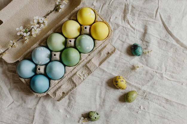 Rustikale Osterwohnung lag Stilvolle Ostereier und blühender Kirschzweig auf rustikalem Tisch Fröhliche Ostern Natürlich bemalte Eier in Papierschale und Frühlingsblüte auf Leinenstoff