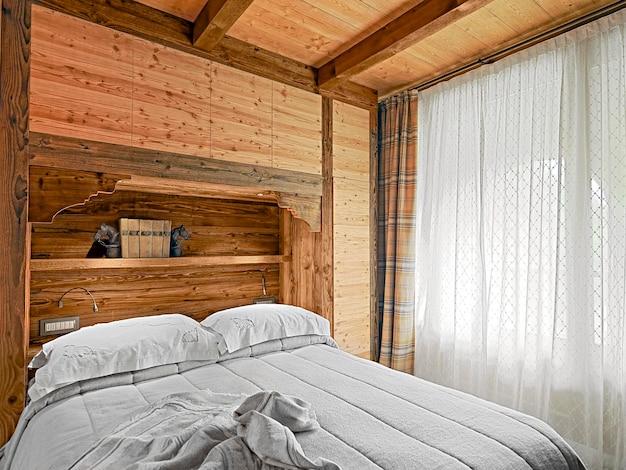 Rustikale Schlafzimmereinrichtung mit Holzvertäfelung und Holzdecke rechts das große Fenster mit Vorhang