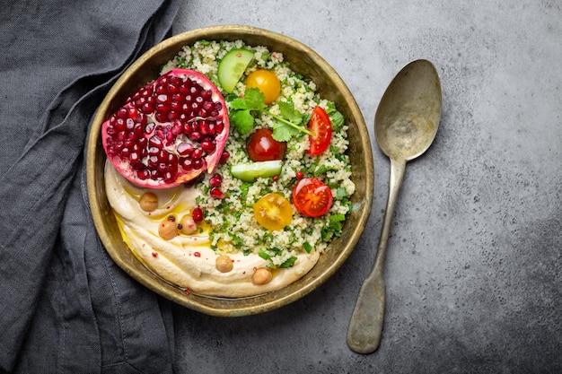 Foto rustikale schüssel mit couscous-salat mit gemüse, hummus und frisch geschnittenem granatapfel. mahlzeit im nahöstlichen oder arabischen stil mit gewürzen und frischem koriander. schönes und gesundes mediterranes abendessen