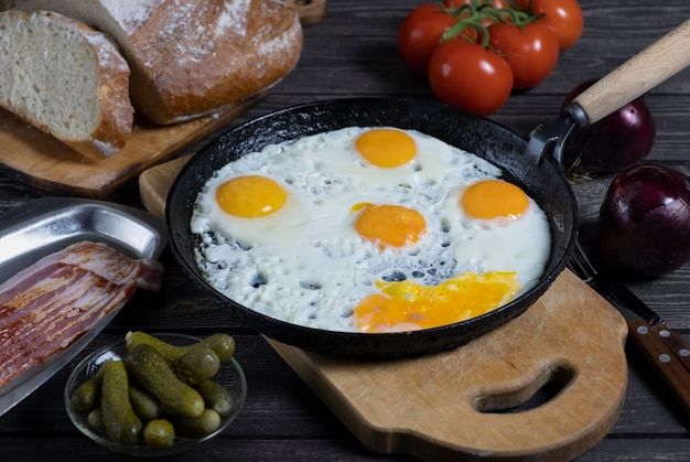 Rustikale Spiegeleier auf einem dunklen Holztisch mit Tomaten, einem Glas Wodka Beacon Brot und eingelegten Essiggurken in einem dunklen Schlüssel