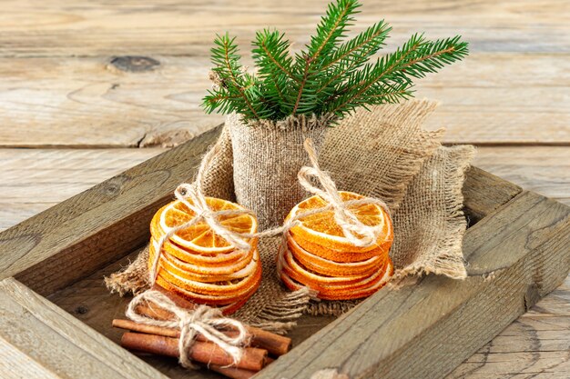 Rustikale Weihnachtskomposition mit getrockneten Orangen, Zimtstangen und Tannenzweigen in einer Holzkiste.