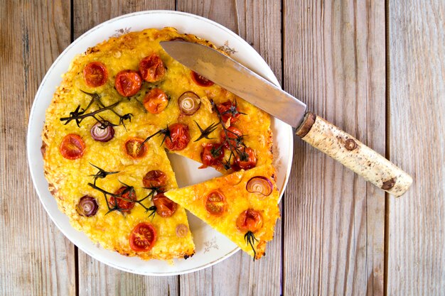 Rustikaler Kuchen mit Käse- und Kirschtomaten auf einem Holztisch.