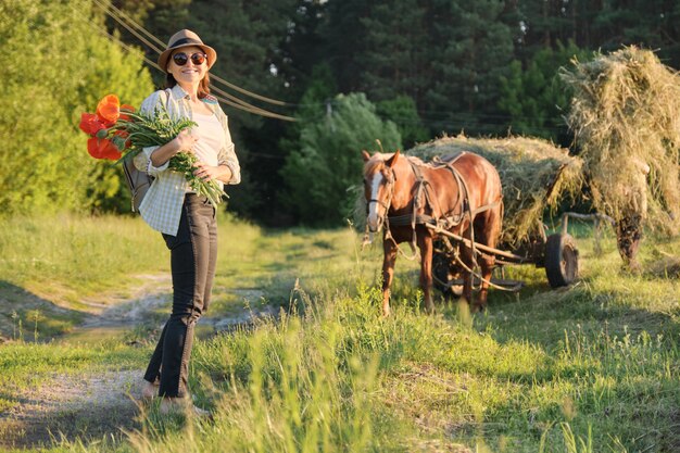 Rustikaler Stil, reife glückliche Frau im Hut mit Blumensträußen von Mohnblumen