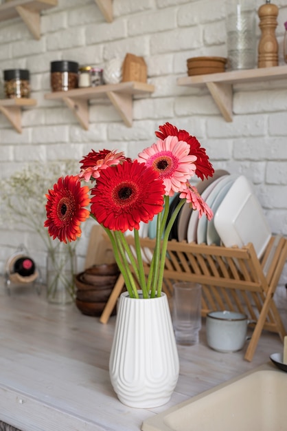 Rustikaler weißer Kücheninnenraum mit roten frischen Gerberablumen in einer weißen Vase