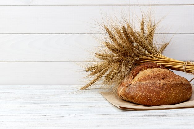 Rustikales Brot und Weizen auf einer alten Weinlese planked hölzerne Tabelle. Freitextraum