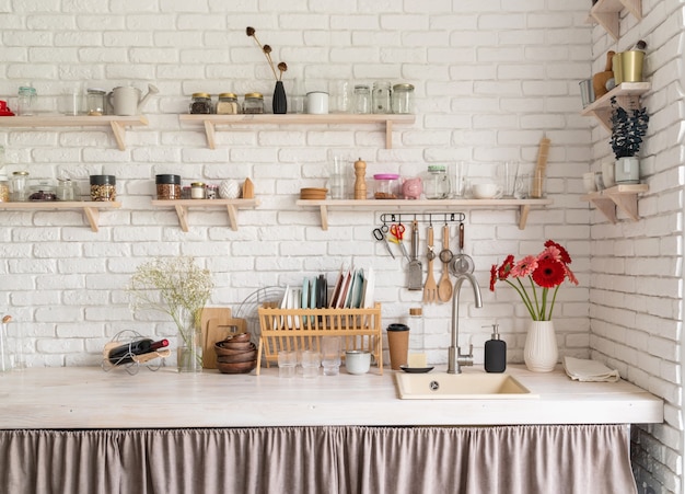 Rustikales Kücheninterieur mit weißer Backsteinmauer und weißen Holzregalen. Frische Gerberablüten