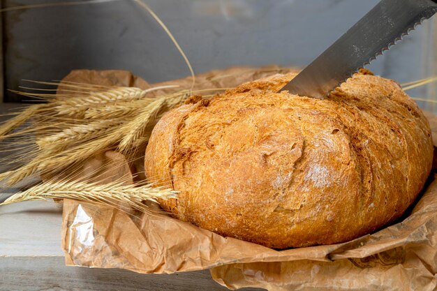 Rustikales traditionelles Dorfbrot mit Holzschneidemesser mit Weizenähren auf Holzhintergrund