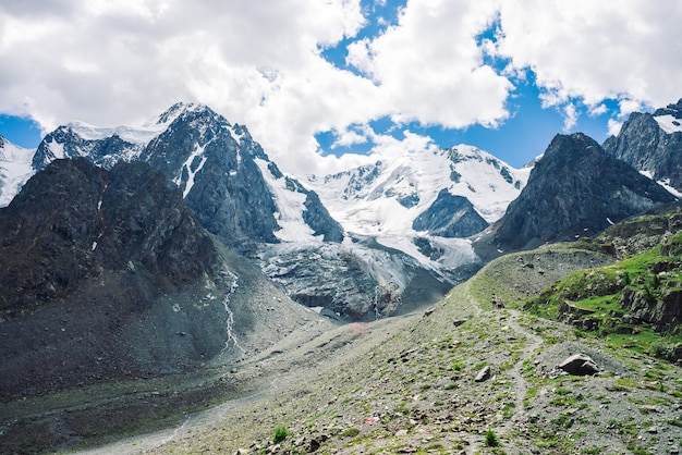 Ruta de senderismo conduce a enormes montañas nevadas en un día soleado. Maravilloso glaciar en la luz del sol. Corrientes de agua en la montaña. Rica vegetación de las tierras altas. Paisaje minimalista soleado atmosférico de la naturaleza.