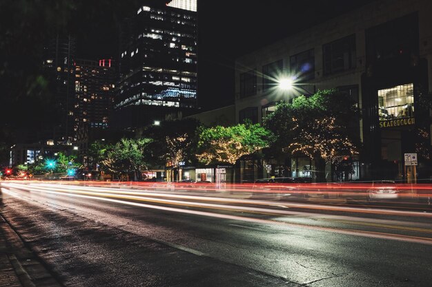 Foto rutas de luz en la carretera por edificios iluminados por la noche