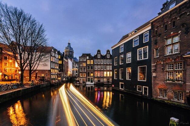 Foto rutas de luz en el río en medio de edificios iluminados en la ciudad contra el cielo al anochecer