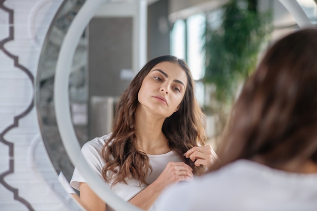 Rutina de belleza. Una mujer revisando las puntas de su cabello cerca del espejo.