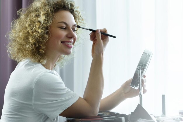 Rutina de maquillaje en casa. Mujer hermosa joven aplicando sombra de ojos con un pincel de maquillaje