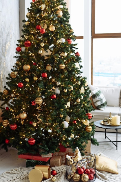 Árvore de Natal com bolas vermelhas e douradas e luzes de guirlanda de ouro em uma sala iluminada.