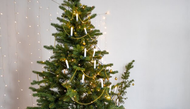 Árvore de Natal com enfeites dourados e uma guirlanda em forma de velas. Iluminação festiva em uma árvore festiva. Feriado de ano novo.