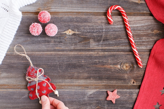 Árvore de Natal de linho com corações nos dedos da mão, bastão de doces, pequenas maçãs de açúcar de neve, xadrez de lã branca e toalha de mesa vermelha com estrelas em uma mesa de madeira rústica