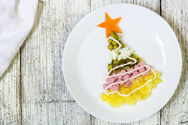 Árvore de Natal de uma salada de olivier no prato sobre uma mesa de madeira branca. Vista superior com um espaço de cópia.