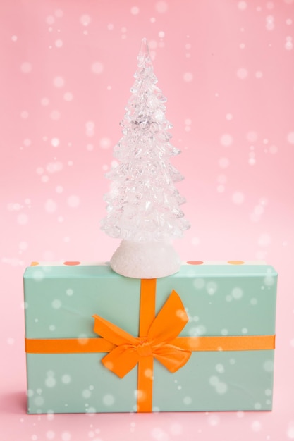 Árvore de Natal de vidro em uma caixa verde com um laço laranja em um fundo rosa