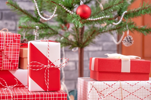 Árvore de Natal decorada com lindos presentes vermelhos e brancos embrulhados em casa com parede de tijolo preto, conceito de design festivo, close-up.