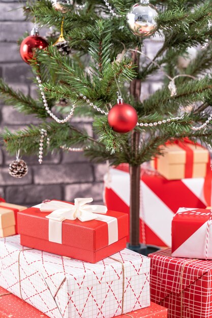 Árvore de Natal decorada com lindos presentes vermelhos e brancos embrulhados em casa com parede de tijolo preto, conceito de design festivo, close-up.