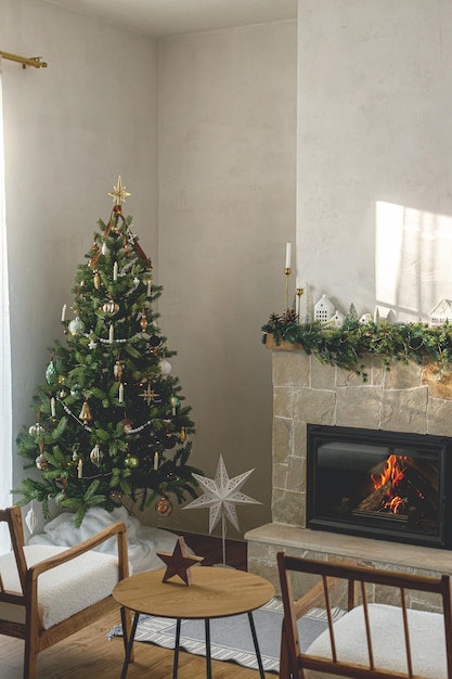 Árvore de natal decorada elegante com bugigangas vintage e decoração moderna na cornija da lareira com sinos e fita Sala de estar escandinava de Natal moderna Véspera de Natal atmosférica