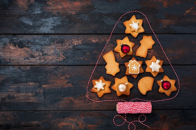 Árvore de Natal feita de biscoitos de gengibre com brinquedos e fita vermelha em uma superfície de madeira velha