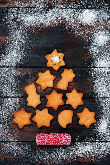 Árvore de Natal feita de biscoitos de gengibre com brinquedos e fita vermelha na superfície de madeira velha. Vista do topo