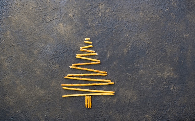 Árvore de Natal feita de biscoitos de palhas pepero, sobre fundo preto de textura. Vista de cima.