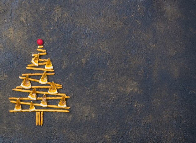 Árvore de Natal feita de biscoitos de palhas pepero, sobre fundo preto de textura. Vista de cima.